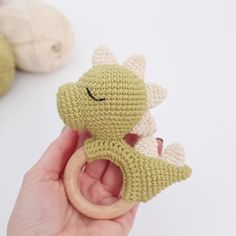 a hand holding a crocheted toy in front of balls of yarn