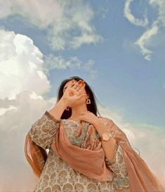 a woman sitting on top of a wooden chair under a blue sky filled with clouds