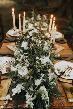 the table is set with white flowers and greenery, candles are lit in the background