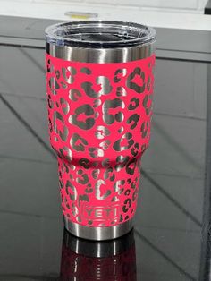 a pink leopard print tumbler cup sitting on top of a black table next to a window