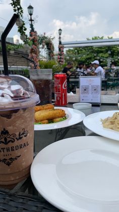 two plates with food on them sitting next to a drink and some other items in the background