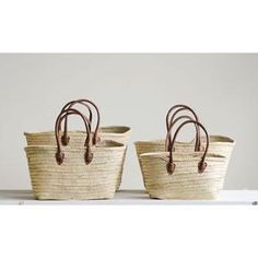 two woven baskets sitting on top of a white table next to each other with brown handles