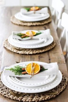 the table is set with white plates and orange slices on them, along with greenery