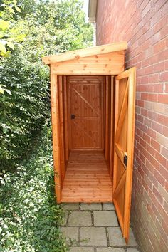 a small wooden outhouse sitting next to a brick wall and green bushes on the side