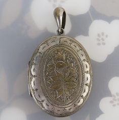 A lovingly hand engraved floral fruit design tops this antique late Victorian silver plated oval locket. The carved design has large leaves, fruit or flower buds, cross hatching, zig-zags and an elegant trim border. The top is fitted with an old large bail. The back is plain.  The locket opens with a fingernail groove and closes with nice snap. The inside has one attached frame on the right side with 37mm x 29mm window. The locket measures 60mm (2 3/8 inches) long with the bail by 34mm (1 3/8 inches) at widest. It weighs 16.4 grams. There is general age wear to the locket with expected fine hairline scratches and tiny dings. There is obvious loss of silver finish with brass peaking through on all parts of the locket, as photographed. This aged quality shows its authenticity and intriguing Tiny Locket, Glass Store, Cross Hatching, Oval Locket, Fruit Design, Flower Bud, Locket Necklace, Hand Engraving, Hand Blown Glass