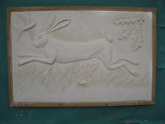 a carving of a rabbit running in the grass with a bird flying above it on a green wall