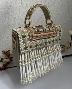 Introducing the Danika Flap Bag, a stunning fusion of bridal elegance and Indian craftsmanship. Hand-beaded with luxurious velvet in enchanting hues of mint, white, and peach, with a beautiful pearl motif, this bag embodies opulence and tradition. Its intricate design, coupled with delicate white suede accents, makes it a standout accessory for brides and lovers of Indian fashion alike. Whether for a wedding ceremony or a cultural celebration, the Danika Flap Bag adds a touch of regal charm to a Bohemian Embroidered Bags For Reception, Designer White Embroidered Bag, White Embellished Clutch Bag, Luxury Embellished Cream Bags, Hand Embellished White Clutch Bag, White Hand Embellished Clutch Bag, Bohemian Cream Beaded Bag, Luxury Bag With Pearl Embroidery For Reception, White Beaded Bohemian Shoulder Bag