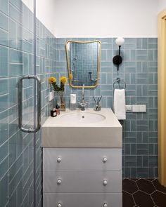 a bathroom with blue tile walls and white counter top, mirror above the sink on the wall