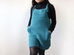 a woman standing in front of a white wall wearing a blue crocheted apron