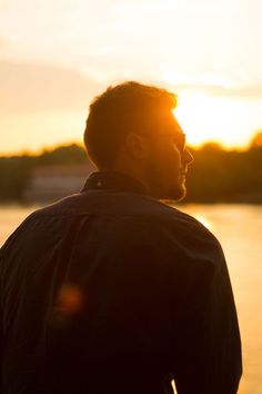 a man is standing in front of the water with his head turned to the side