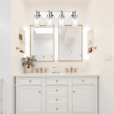 a white bathroom with two sinks and three mirrors on the wall next to each other