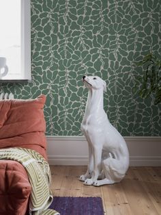 a white dog statue sitting on top of a wooden floor next to a green wall