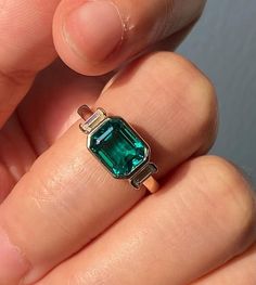 a person is holding a ring with an emerald stone in it's middle finger