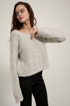 a woman wearing a white sweater and black pants is posing with her hands on her hips