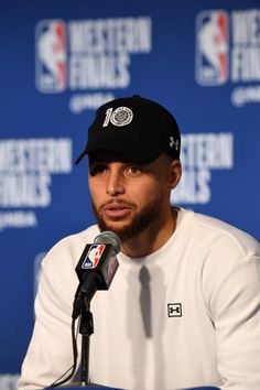 a man in a black hat and white shirt is sitting at a table with a microphone