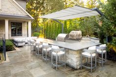 an outdoor kitchen and grill area with white chairs