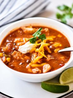 a white bowl filled with chili and cheese on top of a plate next to lime wedges