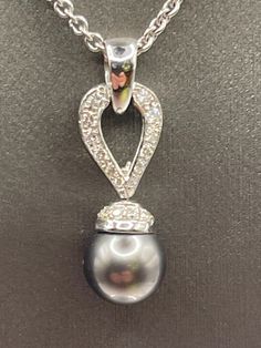 This gorgeous ladies pendant is designed in 18 karat solid white gold.  A genuine 8.6 mm black pearl dangles from a diamond teardrop loop with a round diamond encrusted cup that holds the pearl.  The necklace hangs beautifully on a 14 karat white gold round link chain.  A lovely necklace that can be worn for any occasion.  Tahitian pearls are some of the finest in the world Weight:  7.8 grams Chain Length:  20" TDW-0.55cts Our Price $1498.00 Regularly Priced At $2100.00 Please See Our Video Remember - If you're purchasing for yourself or a gift for a loved one, buy with confidence.  We Guarantee Everything We Sell!  SKU # N745 Pearl And Diamond Necklace, Tahitian Pearls, Lovely Necklace, Black Pearl, Link Chain, Gold Black, Chain Length, Round Diamond, Round Diamonds