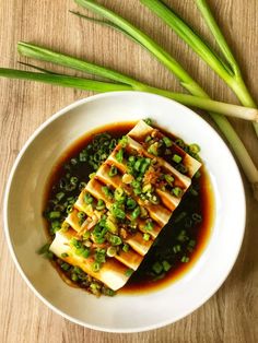 a white plate topped with tofu covered in sauce and green onions on top of a wooden table