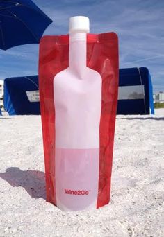 a wine bottle in the sand with an umbrella behind it and a blue sky background