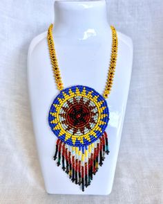 Please Read Full Description This Indigenous beaded necklace showcases a striking sunburst design.  Handcrafted with an array of seed beads in vibrant bold colors.  The central medallion draws attention with its radiating design, reflecting the life-giving power of the sun, creating a beautiful balance of artistry and cultural significance.  This necklace is in great condition.  All of the beads are complete and intact.  The backing of the sunburst shows typical vintage wear.  Please see/zoom photos for a closer look. This necklace is a perfect statement piece that celebrates Indigenous heritage, and brings a touch of history and elegance to any collection.   Measurements:  15 1/2" Long (From top to bottom of the fringe beading). The starburst is 2 1/2" Round (Not including the fringe bead Indigenous Beaded Necklace, Traditional Ceremonial Beaded Necklaces, Native Beaded Medallion Necklace, Traditional Ceremonial Hand-strung Beaded Necklaces, Vintage Blue Hand-strung Beaded Necklaces, Zoom Photo, Vintage Wear, Vintage Finds, Bold Colors