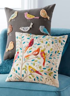 two pillows with birds on them sitting on a blue couch