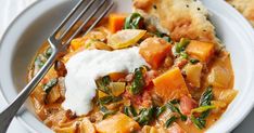 a white bowl filled with stew and vegetables next to a piece of pita bread