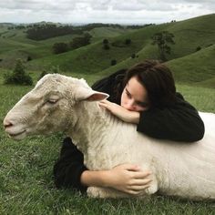 a woman laying on the ground with a sheep in her lap and looking at the camera