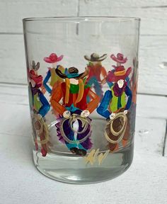 a glass that has some paper cutouts in the shape of people on it, sitting on a table