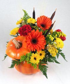 a vase filled with lots of different colored flowers and pumpkin shaped decorations on top of a white table