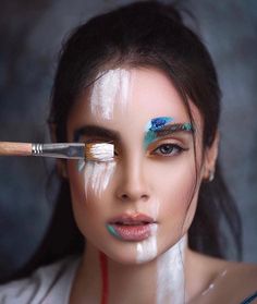 a woman with white paint on her face and two brushes in front of her face