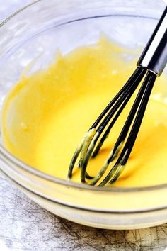 a glass bowl filled with yellow liquid and whisk