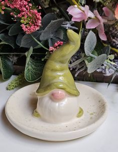 a ceramic figurine sitting on top of a white plate next to some flowers