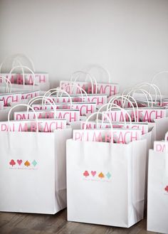 white shopping bags with pink and green designs on them sitting on a wooden floor in front of a wall