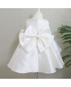 a white dress with a big bow on the front and back, sitting next to a potted plant