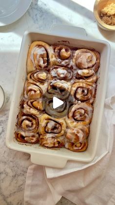 a pan filled with cinnamon rolls sitting on top of a counter next to plates and bowls