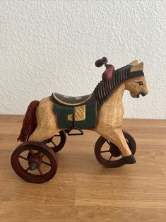 a wooden toy horse pulling a cart on a wood floor with a white wall in the background