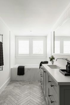 a bathroom with white walls and marble flooring, along with two sinks on either side of the bathtub