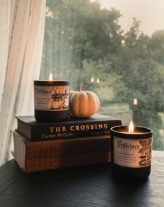 two candles sitting on top of some books next to a window with trees in the background