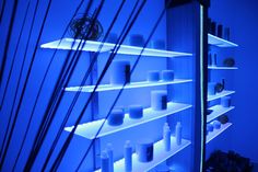 the shelves are filled with many different types of candles and vases in blue light