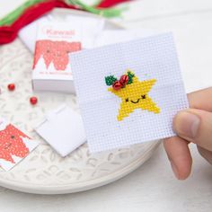 someone holding up a cross stitch card with a yellow star on it and red ribbon