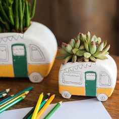 two planters with plants in them sitting on a table next to pencils and paper