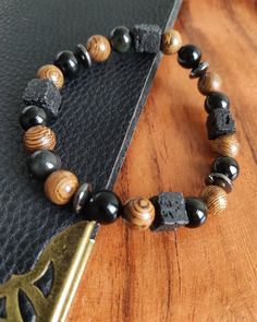 Embark on a journey of spiritual grounding with our meticulously crafted bracelet featuring Obsidian, Cube Lava Stone, Sandal Wood, and Hematite. This unique combination is more than a fashion statement--it's a wearable source of positive energy and balance. Obsidian: Known as the 'Mirror of the Soul,' Obsidian is a protective stone that shields against negativity. Its volcanic origin infuses it with powerful grounding properties, promoting clarity and self-discovery. Cube Lava Stone: Unleash the elemental energy of Cube Lava Stone, symbolizing rebirth and shedding old layers. Its porous surface makes it an ideal carrier for essential oils, enhancing the sensory experience and adding an extra dimension to your journey. Sandal Wood: Sandal Wood beads not only contribute to the bracelet's ea Spiritual Wooden Beads Jewelry For Everyday, Spiritual Jewelry With 108 Beads For Everyday, Everyday Spiritual Jewelry With 108 Beads, Artisan Wooden Beads Bracelets For Meditation, Spiritual Rosary Bracelet With Wooden Beads, Artisan Black Bracelet For Gift, Spiritual Bracelets With 108 Beads For Everyday, Adjustable Spiritual Bracelet With Wooden Beads, Symbolic Beaded Bracelets With Natural Stones For Meditation