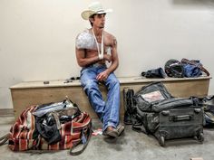 a shirtless man sitting on a bench next to his luggage and other items in the background