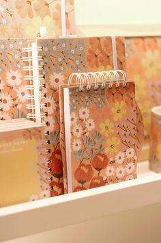 notebooks are lined up on a shelf in a room with floral wallpaper and flowers