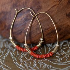 red and gold beaded hoop earrings sitting on top of a wooden table next to a piece of wood