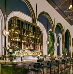 the bar is lined with black leather chairs and gold trimmings, along with tall arched windows