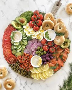 a platter with bagels, tomatoes, cucumbers, onions, olives and other vegetables