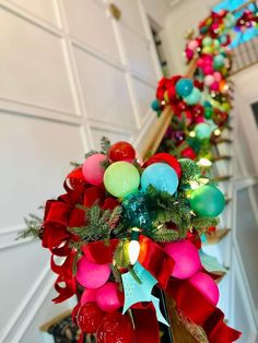 a christmas wreath with ornaments and lights on the top of it in front of a staircase