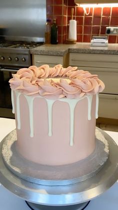 a pink cake with white icing sitting on top of a metal stand in a kitchen